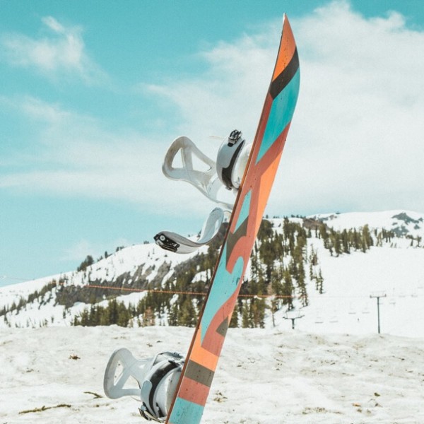 Ein Snowboard steckt vor winterlicher Bergkulisse im Schnee.