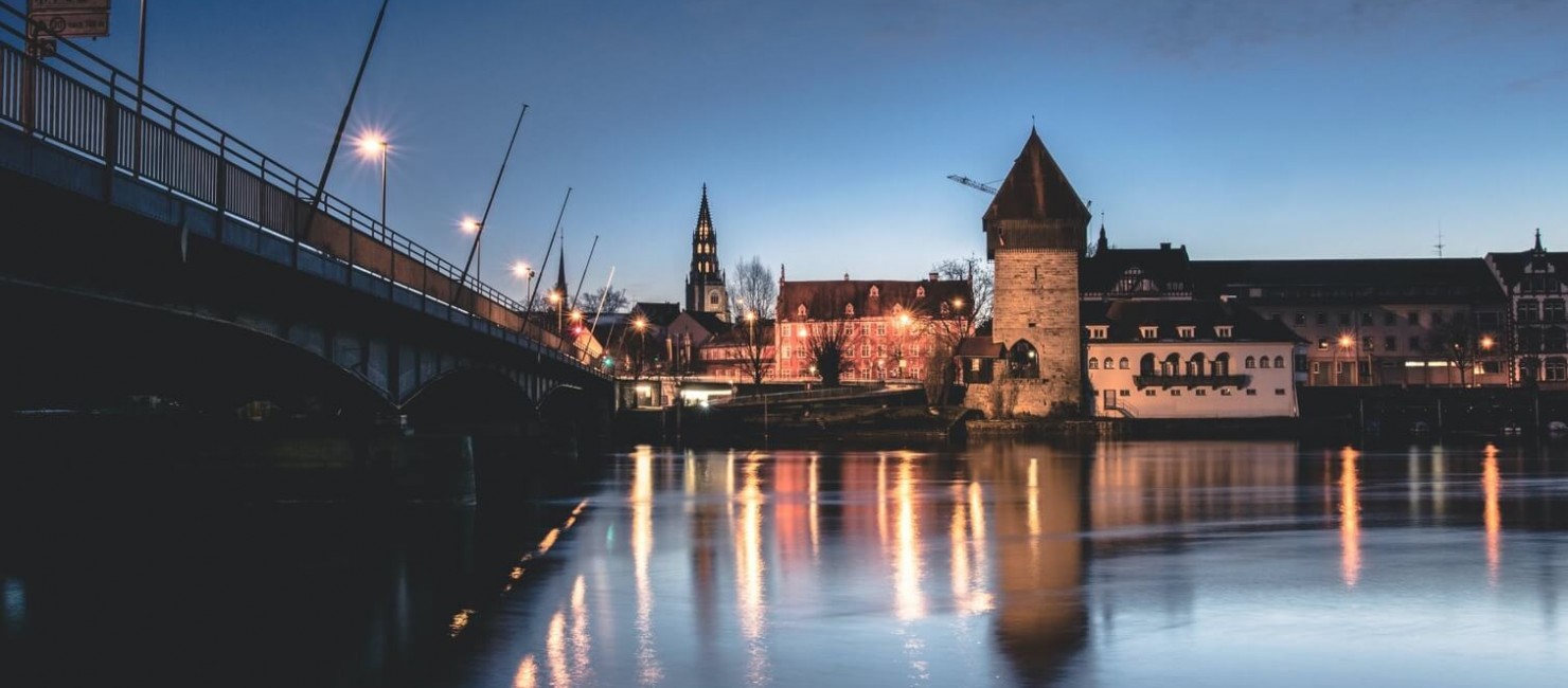 Sicht auf eine atmosphärisch beleuchtete Altstadt vom Fluss aus.