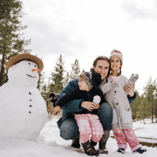 Eine Frau posiert mit 2 Kindern im Winter neben einem Schneemann.