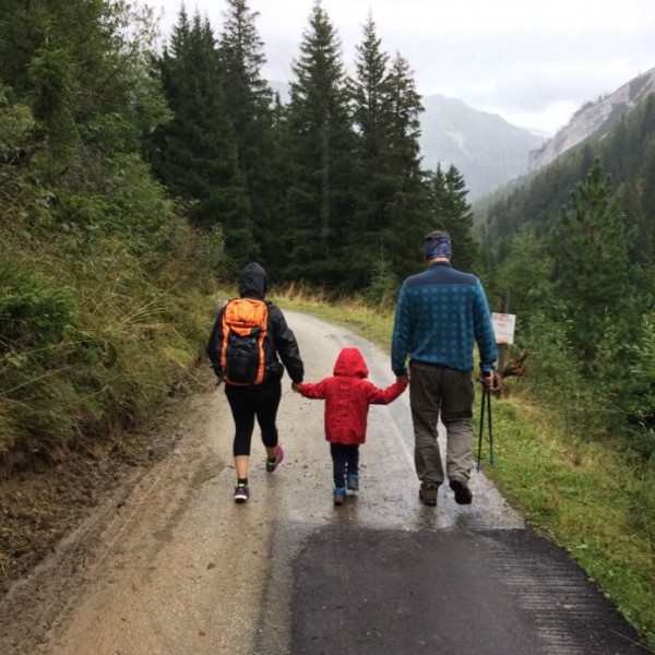 Eine Familie wandert Hand in Hand durch einen regnerischen Wald.